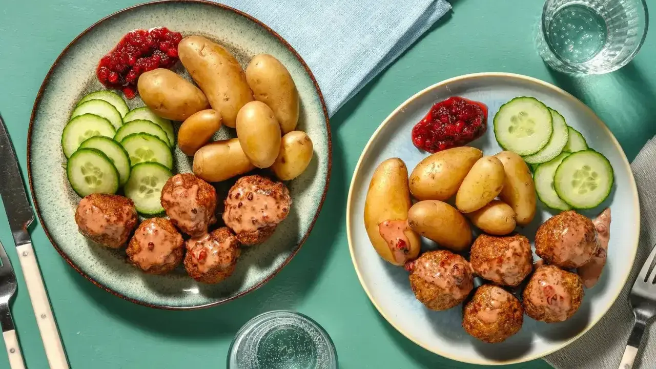 Två tallrikar med köttbullar, småpotatis, gurka och lingonsylt. En perfekt snabb middag för två.