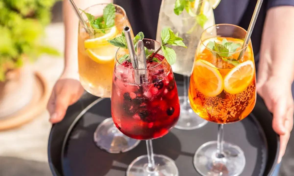 Vier erfrischende Hugo Spritz Cocktails mit Beeren, Zitrusfrüchten und Minze auf einem Tablett.