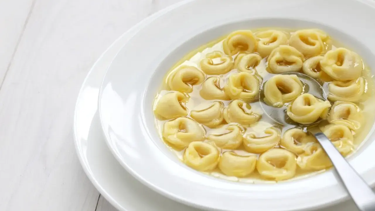 Tortellini in brodo, uno dei cibi tipici dell'Emilia Romagna, serviti in una ciotola bianca con un cucchiaio.