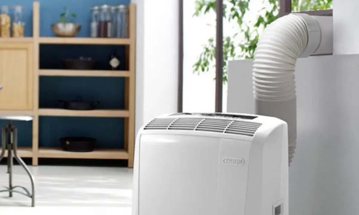 Climatiseur Rowenta portable, avec son tuyau d'évacuation dirigé vers une fenêtre. Un meuble de cuisine est visible à gauche.