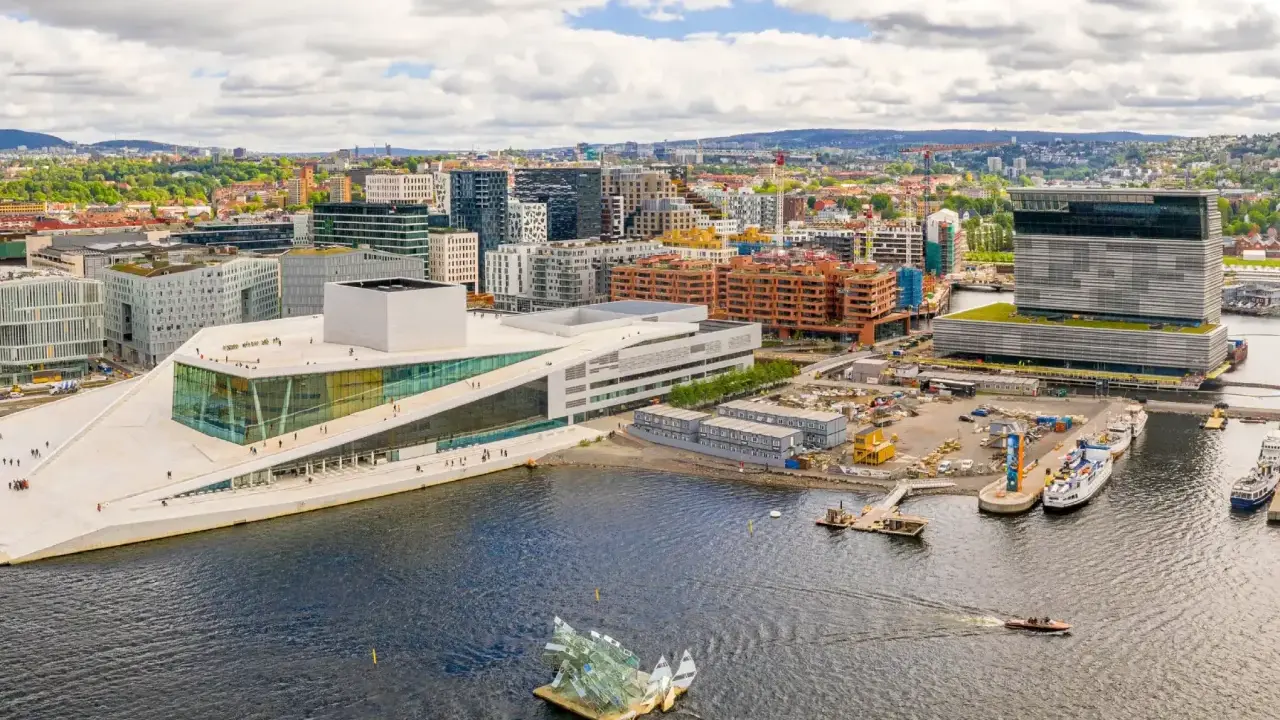 Il porto di Oslo con l'Opera House e moderni edifici. Barche navigano nell'acqua scura.