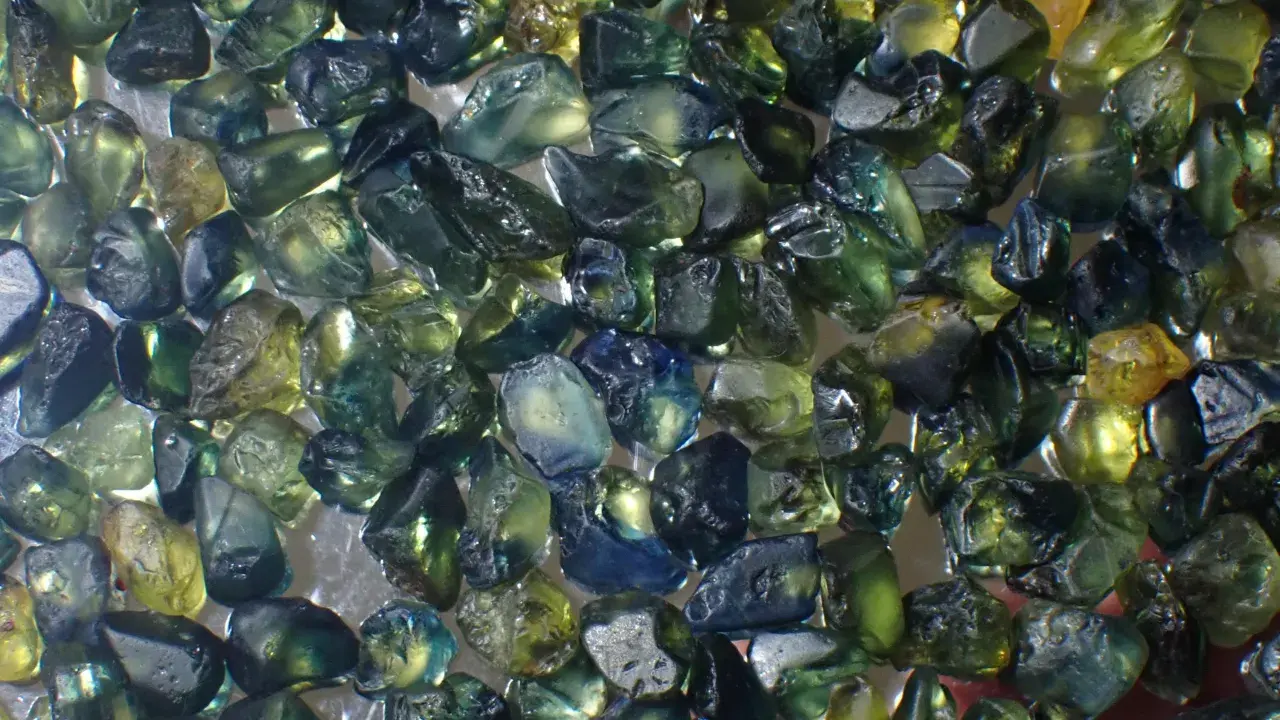 Un mucchio di zaffiri grezzi australiani, con sfumature verdi, blu e gialle. Il loro valore è legato alla rarità e alla bellezza di queste gemme naturali.
