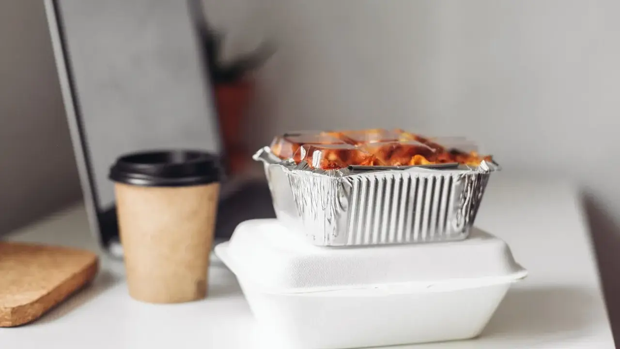 Gotowe jedzenie na wyjazd: zapiekanka w folii aluminiowej i kawa w kubku. Idealne na szybki lunch przy laptopie.