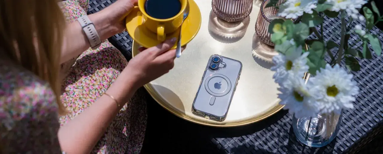 Eleganckie etui przezroczyste z wzorami na telefon, leżące obok żółtej filiżanki kawy i białych kwiatów.