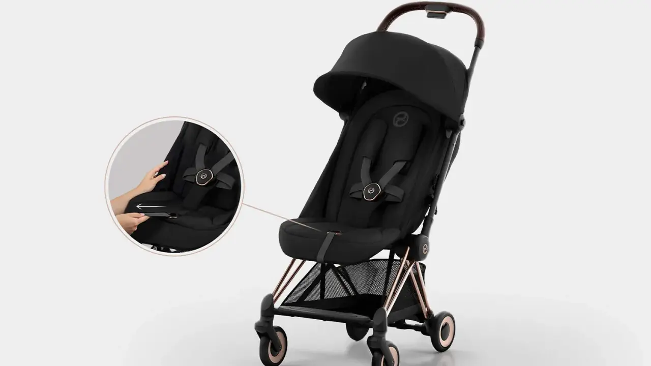 Elegancki czarny wózek Cybex Coya z miedzianymi detalami. Widoczna lupa pokazuje łatwe zapinanie pasów.