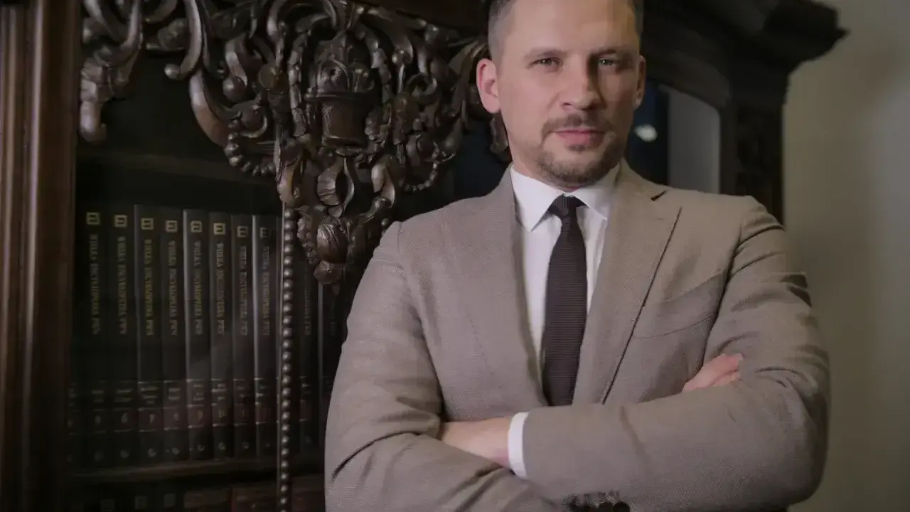 Mężczyzna w garniturze stoi przed regałem z książkami prawniczymi.