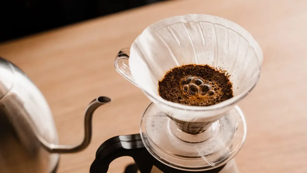 Frisch aufgebrühter Kaffee blubbert im Papierfilter. Ein Wasserkocher steht bereit, um das Ritual des Kaffeefilter selber machen zu beginnen.