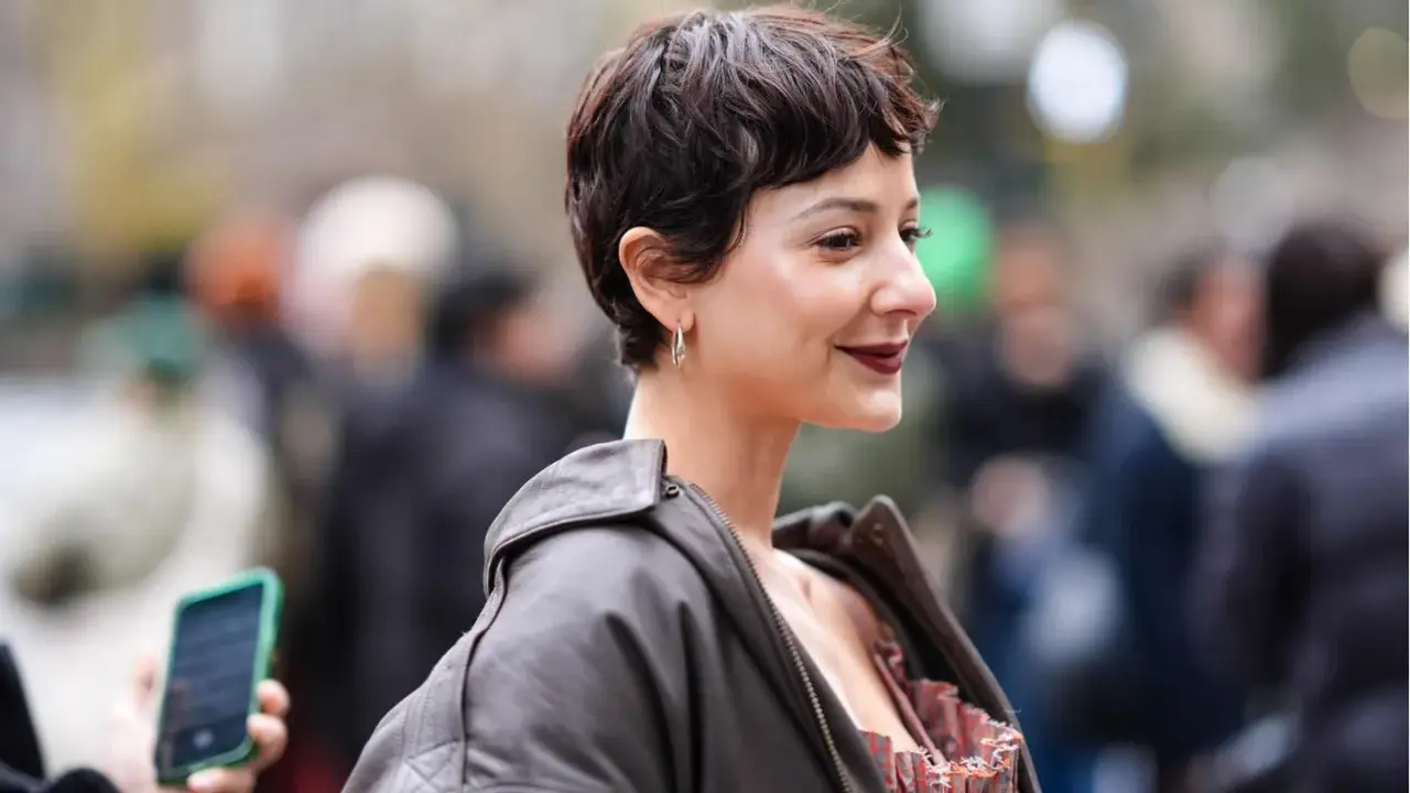 Frau mit einem lässigen Pixie-Cut, dunklem Lippenstift und Lederjacke lächelt in die Kamera.