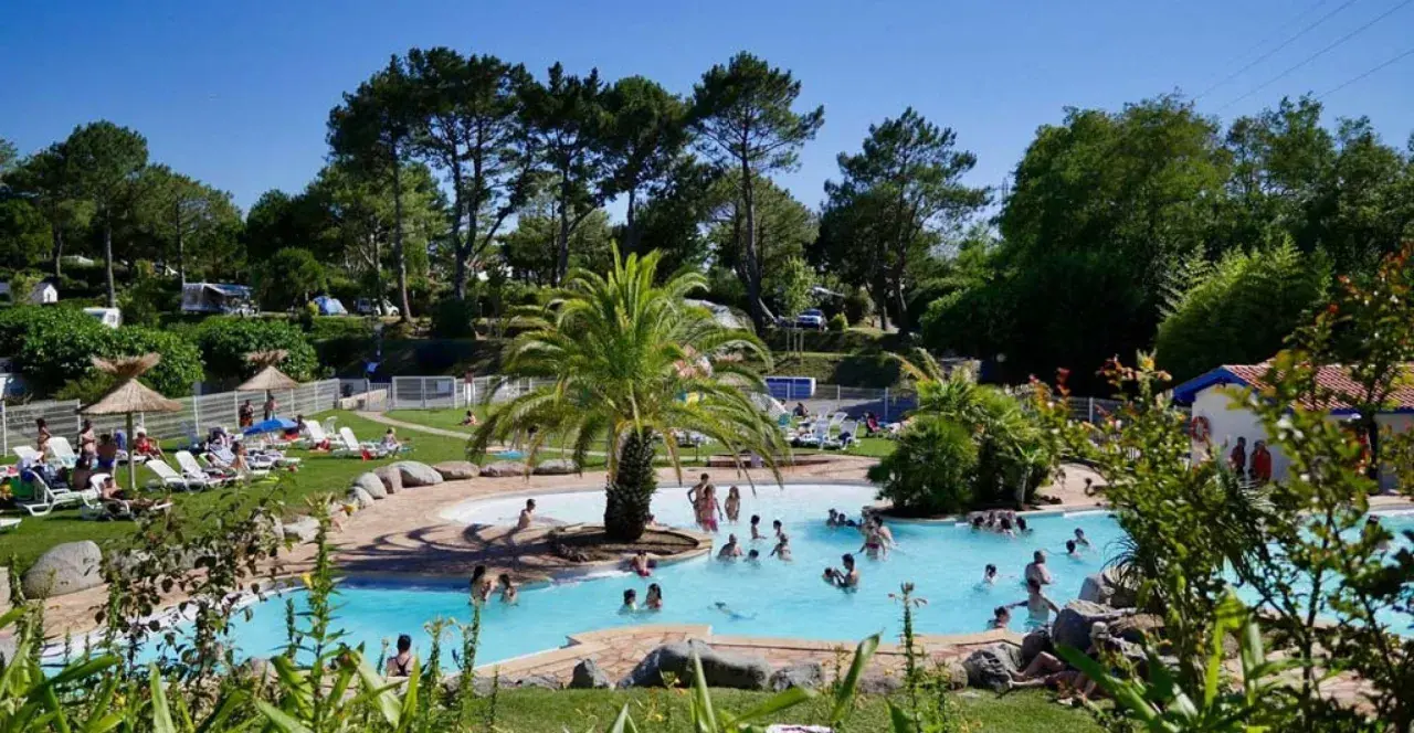 Disfruta de un día soleado en el camping de País Vasco, con una piscina refrescante y gente relajándose en tumbonas.