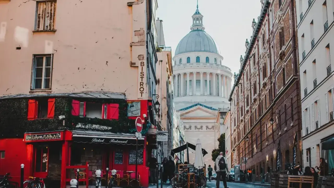 Urokliwa uliczka w paryskiej dzielnicy łacińskiej z czerwonym bistro i majestatycznym Panteonem w tle.