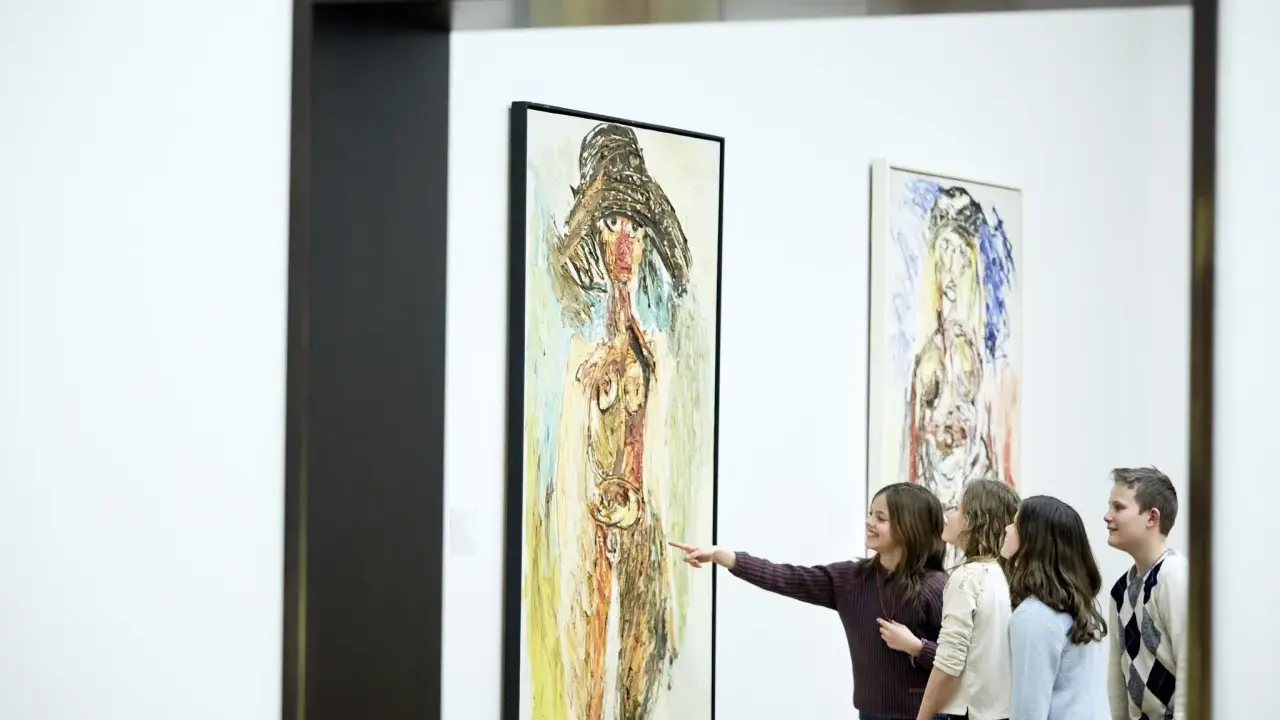 A group of children admire a painting in the style of the cobra art movement, with one girl pointing at the abstract figure.