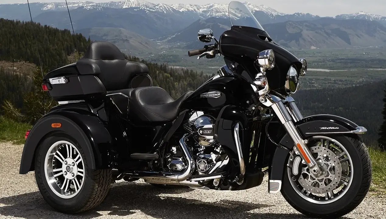 Harley-Davidson negro de tres ruedas aparcado en un paisaje montañoso. Recuerda que las motos de tres ruedas necesitan carnet de moto.
