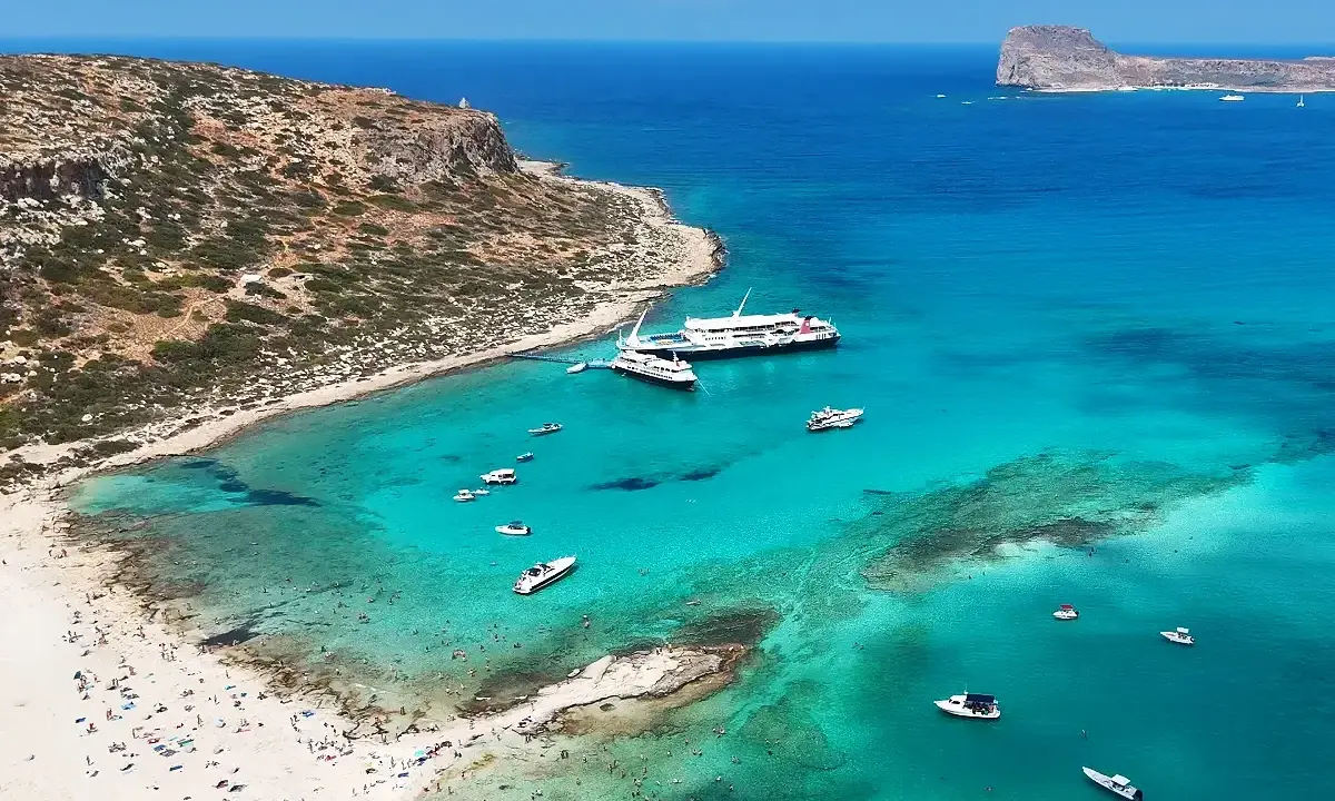 Rajska plaża z turkusową wodą, statkami i ludźmi. Kreta wschodnia atrakcje zachwycają!