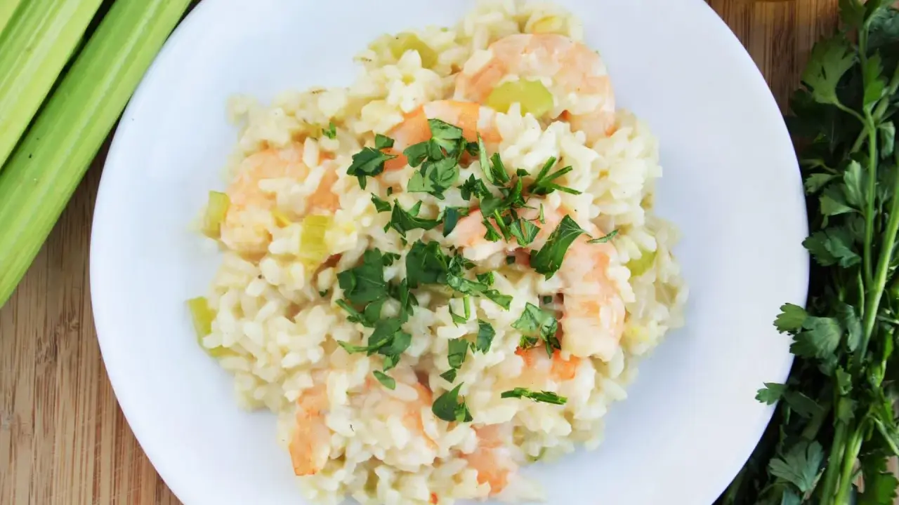 Pyszne risotto z krewetkami, udekorowane natką pietruszki, obok łodygi selera i oliwy.