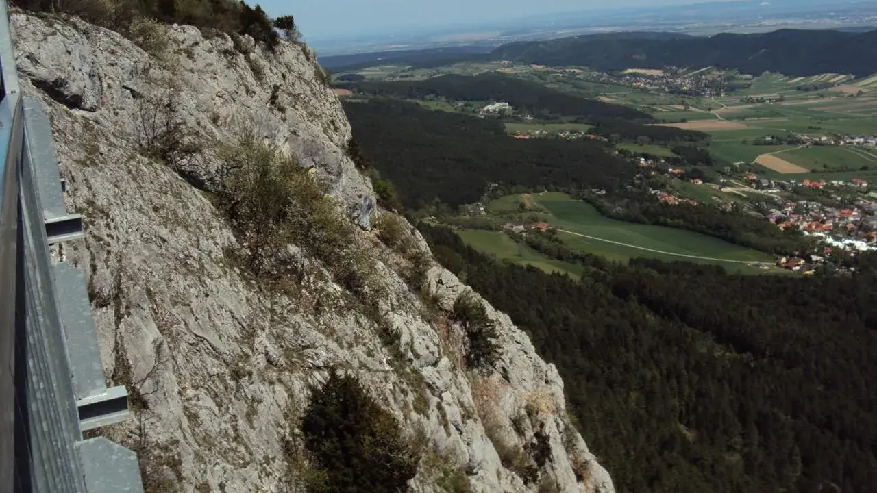 Widok z **Hohe Wand** na dolinę z lasami i wioskami. Stroma, skalista ściana po lewej stronie.