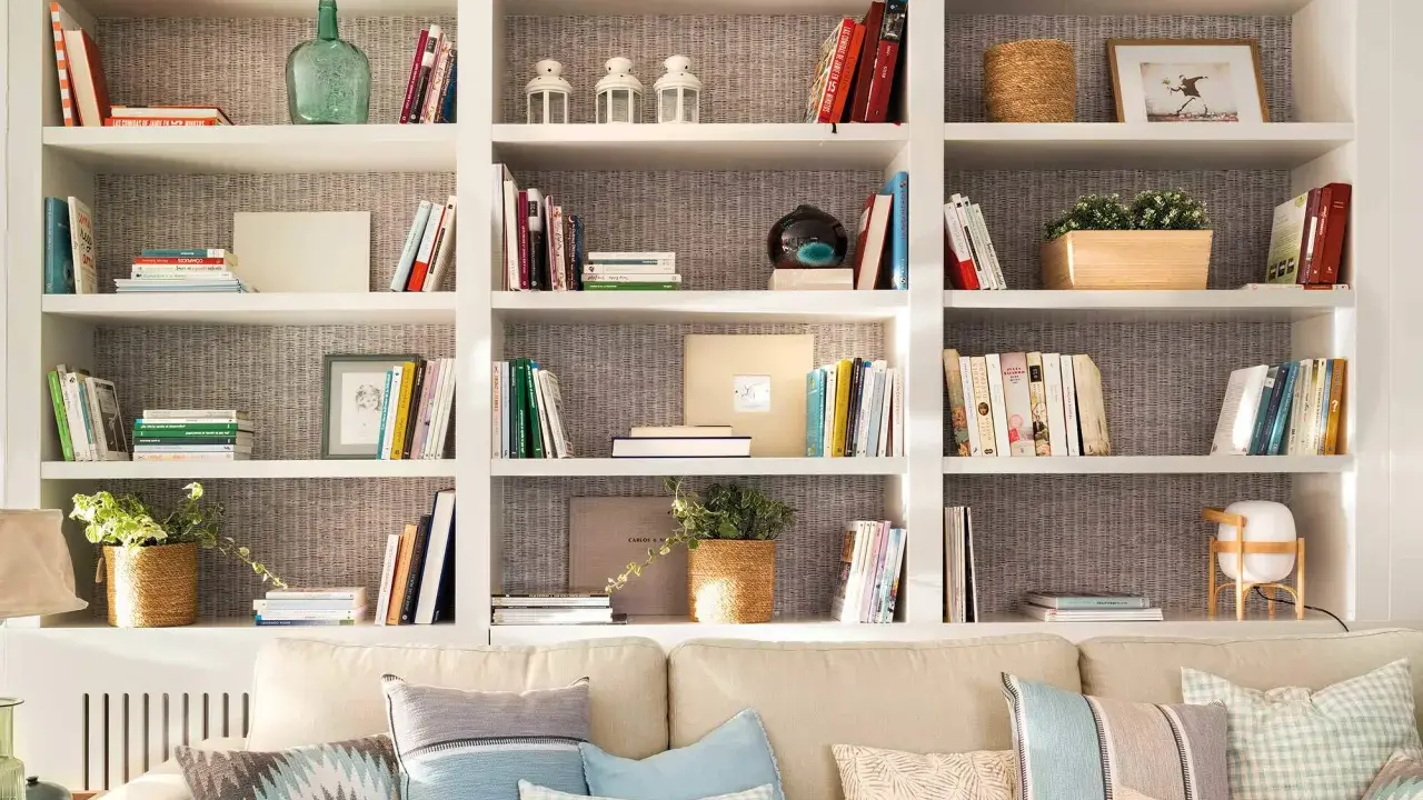 Estanterías blancas llenas de libros, plantas y objetos decorativos. Una idea de **qué poner detrás del sofá** para crear un rincón acogedor y lleno de estilo.
