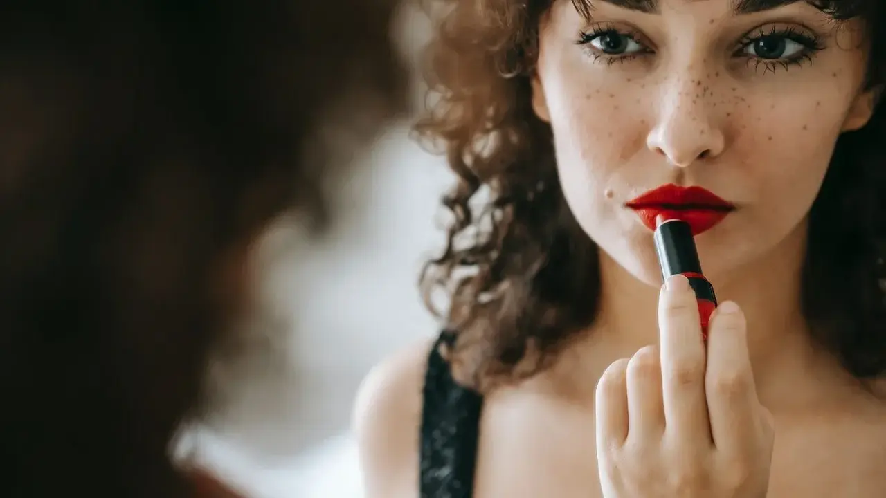 Donna con capelli ricci applica un trucco con rossetto rosso vibrante, creando un look audace e seducente.