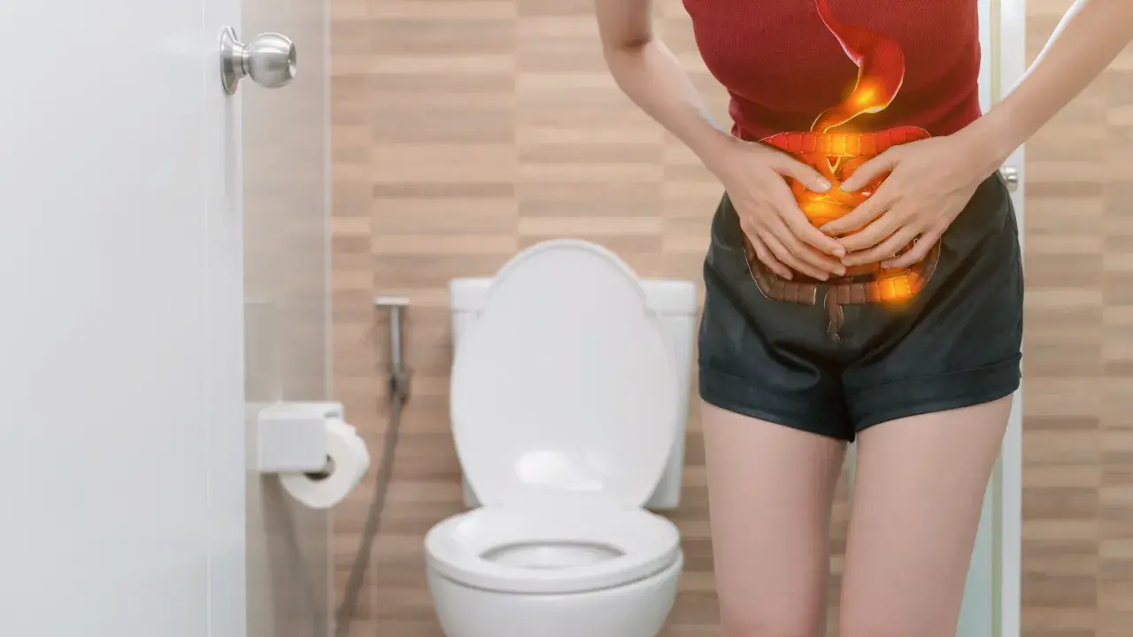 Mujer con dolor abdominal, con ilustración del sistema digestivo en rojo y naranja, frente a un inodoro.