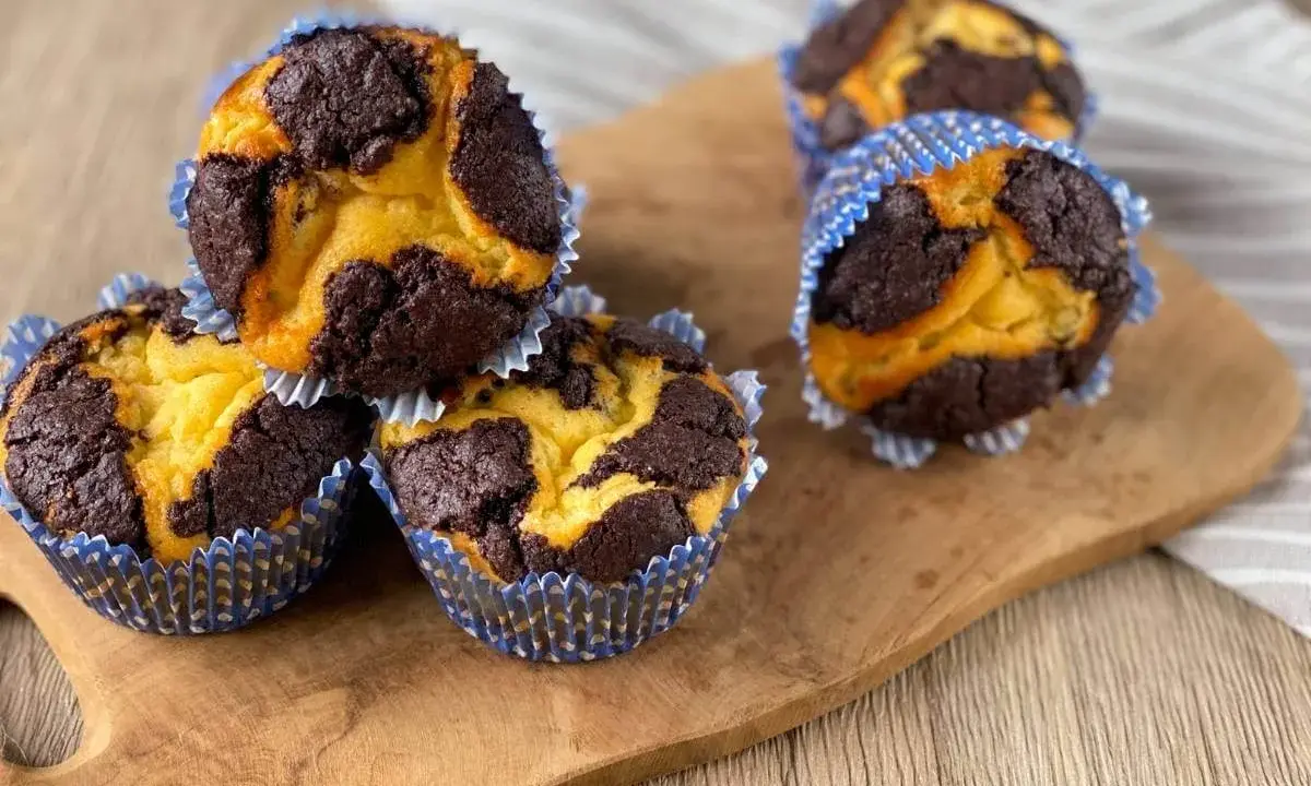 Schokoladen-Vanille-Zupfkuchen-Muffins in blauen Papierförmchen auf einem Holzbrett.