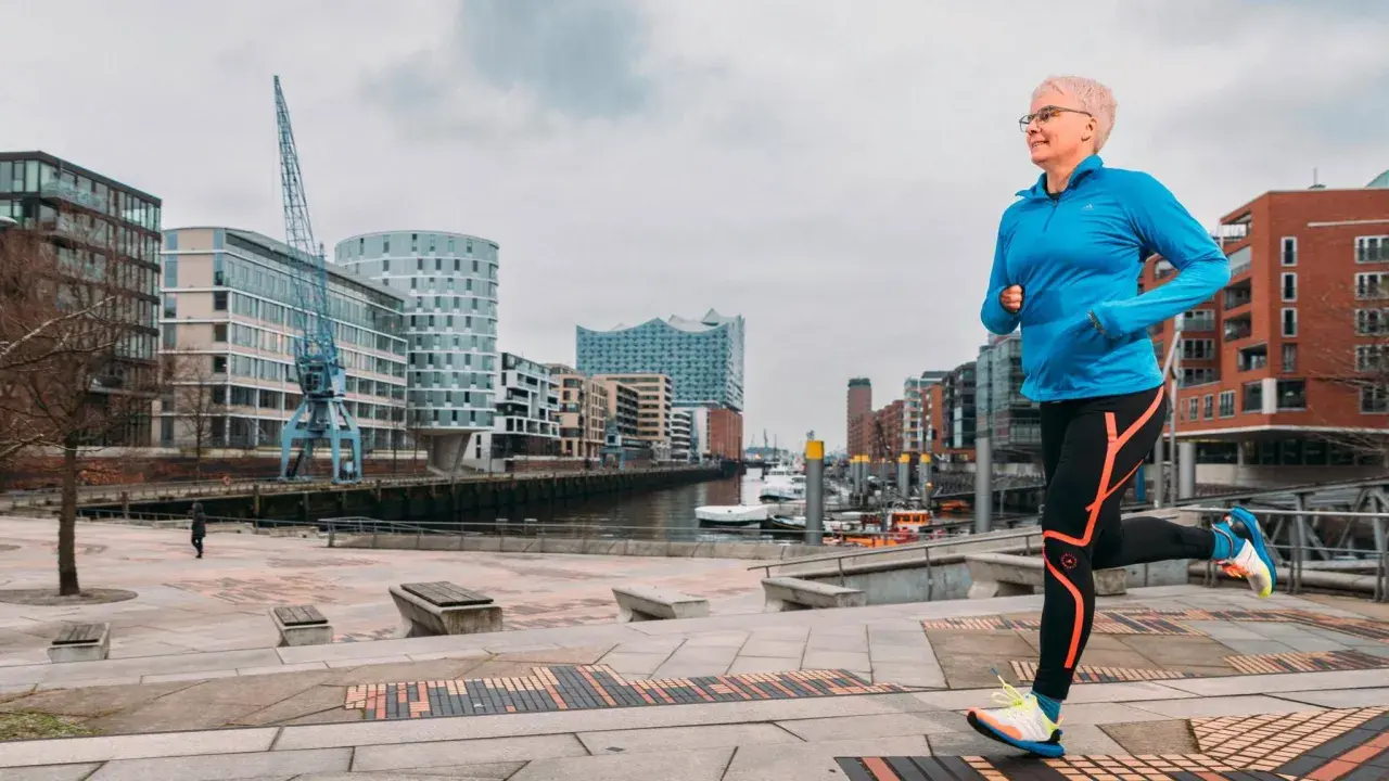 Frau mit kurzen Haaren läuft im Hafen. Sie trägt Sportkleidung und Schuhe. Mit Laufen abnehmen ist ihr Ziel.