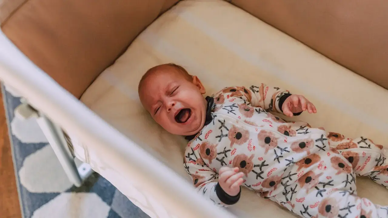 Bebé llorando en su cuna, con un pijama de koalas. Un momento difícil para dejar llorar a un niño de 2 años para dormir.