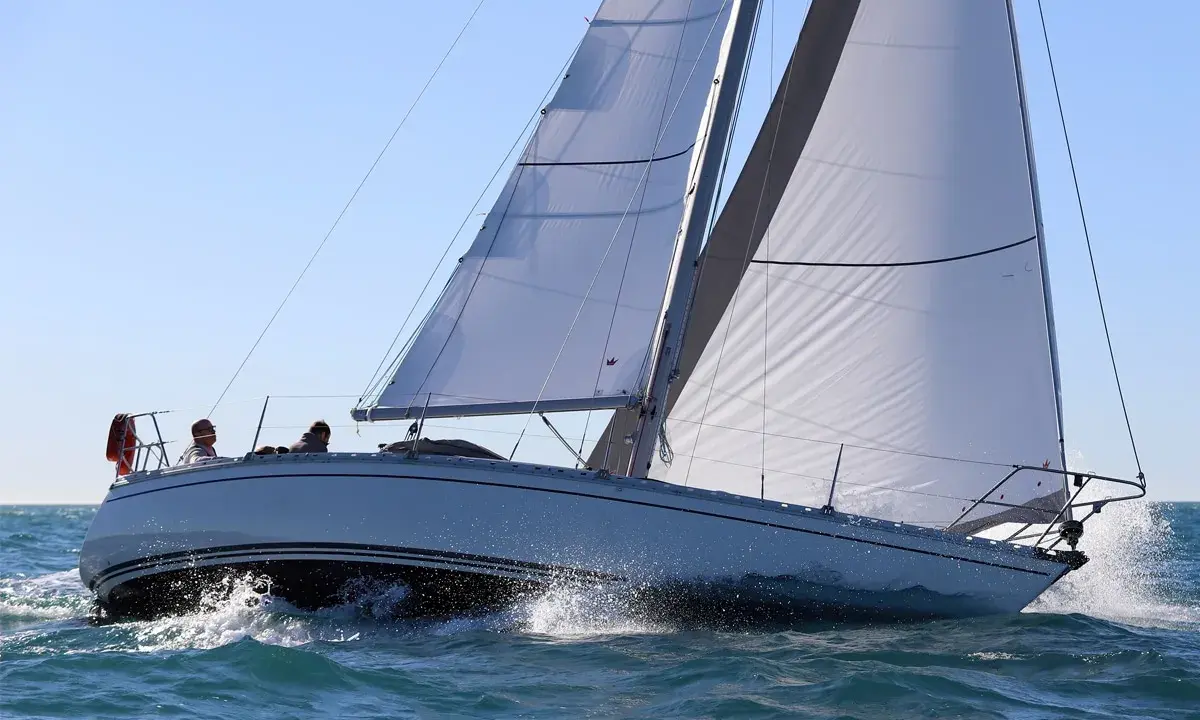 Un voilier Jeanneau Symphony navigue sur une mer agitée, ses voiles blanches gonflées par le vent. Un avis positif pour ce bateau.
