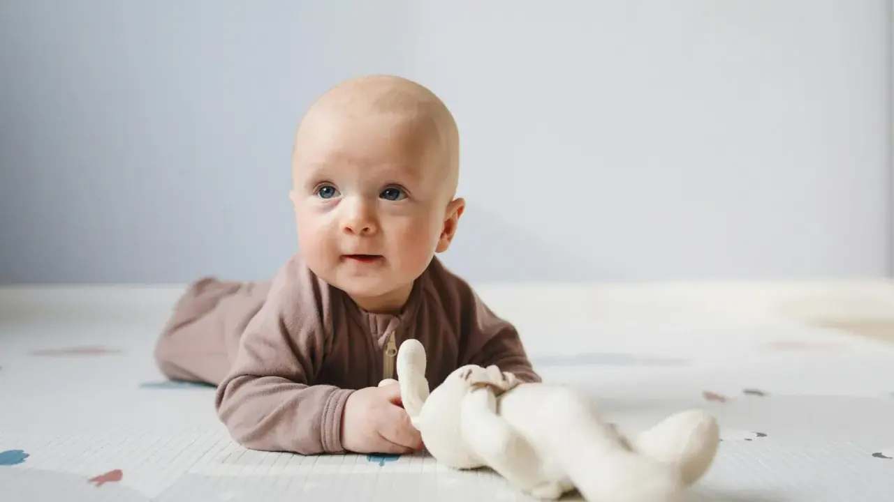 Söt bebis på mage med en mjuk kanin. Bebis mage storlek verkar perfekt för lek och utforskning.