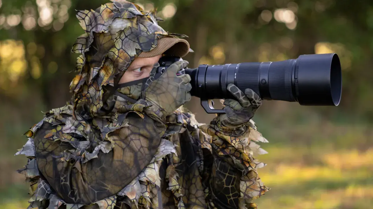 Fotograf w ghillie suit z aparatem do fotografowania zwierząt czeka na idealny kadr.