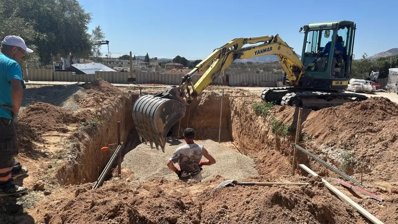 Excavadora amarilla trabajando para cavar zanjas en un día soleado. Un hombre supervisa la obra.