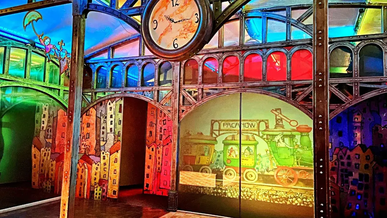 Kolorowa sceneria z pociągami i bajkowymi postaciami, idealna na pacanów atrakcje dla dzieci. Zegar nadaje miejscu magiczny klimat.