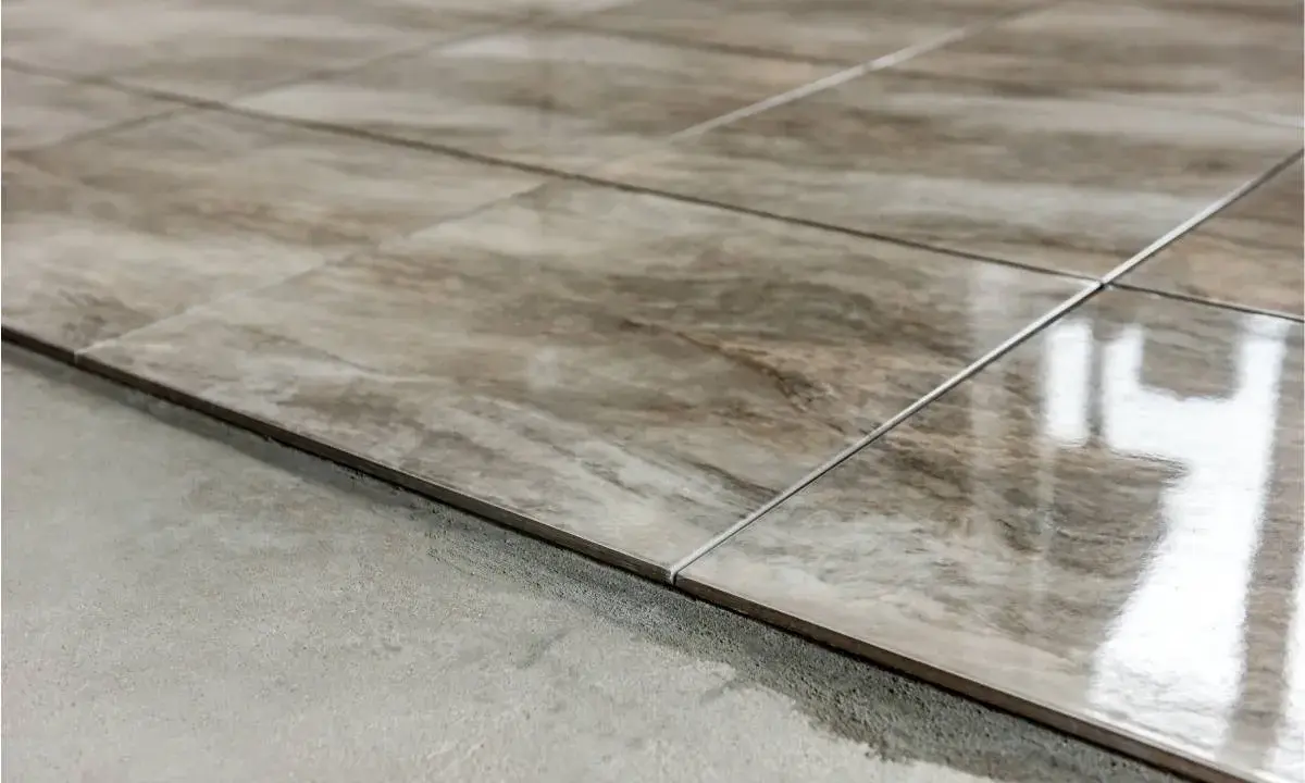Detalle de las partes de un piso: baldosas de cerámica con veteado marrón y gris, recién colocadas sobre una base de cemento.