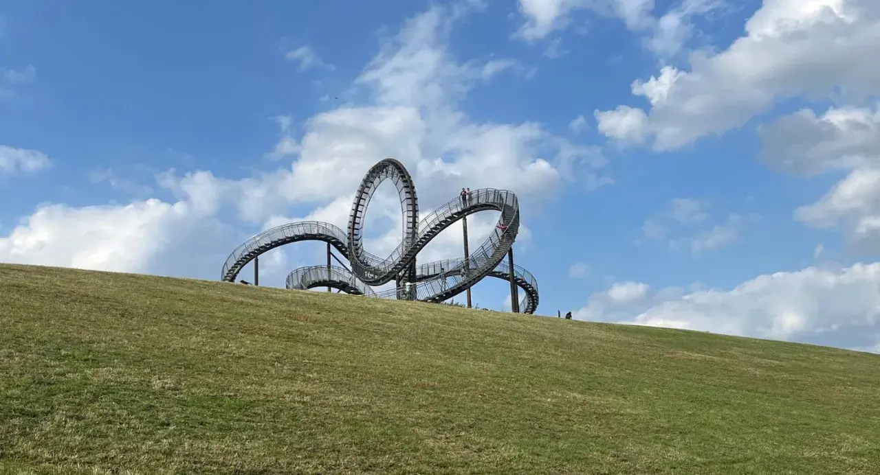 Ein skulpturales Kunstwerk auf einem Hügel, das an eine Achterbahn erinnert. Perfekt für spannende Ausflugsziele mit Kindern.