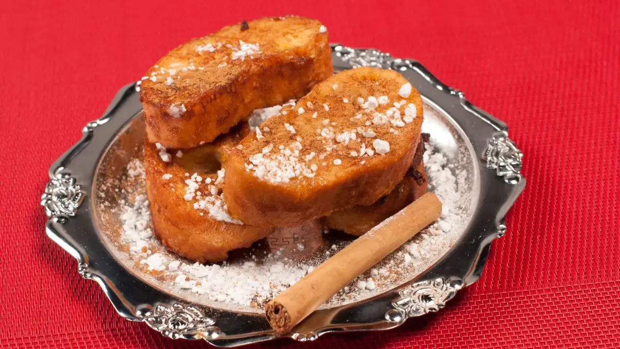 Torrijas de Semana Santa espolvoreadas con azúcar glas y canela, servidas en un plato plateado con una rama de canela.