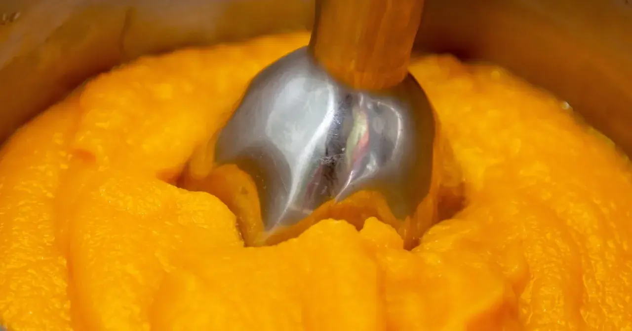 Metalowa końcówka blendera zanurzona w gęstym, pomarańczowym puree z dyni.