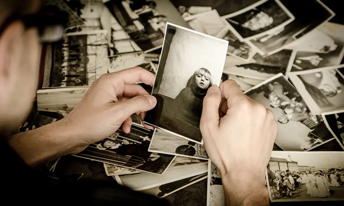 Ręce przeglądają stare fotografie, tworząc osobistą archiwizację zdjęć. Widać portret dziecka i grupowe ujęcia.
