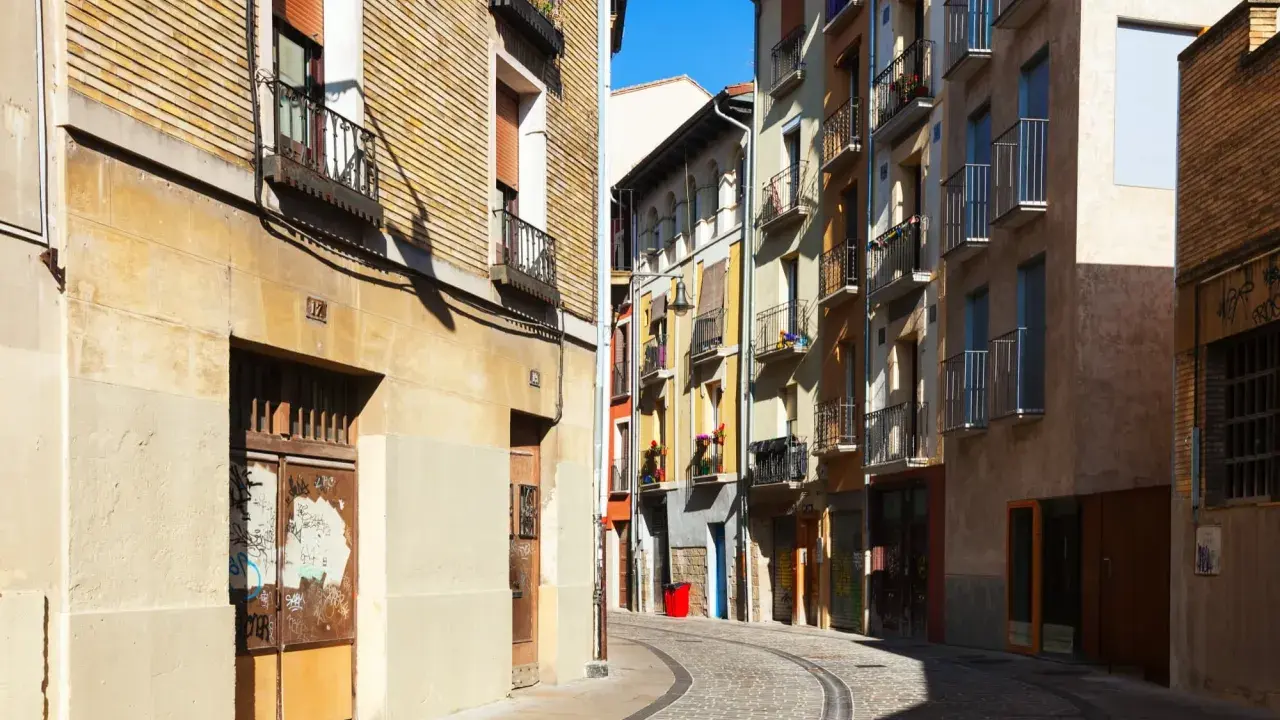 Calle adoquinada con edificios coloridos y balcones. Un cartel de "haya real estate" podría estar en uno de estos locales.