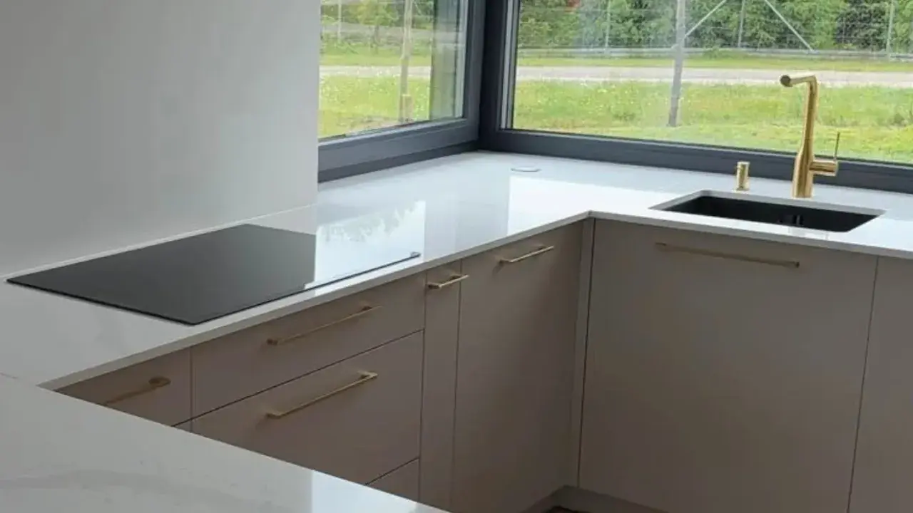 Nowoczesna kuchnia z blatem z **neolith spieki**. Złota bateria i czarny zlew przy dużym oknie.