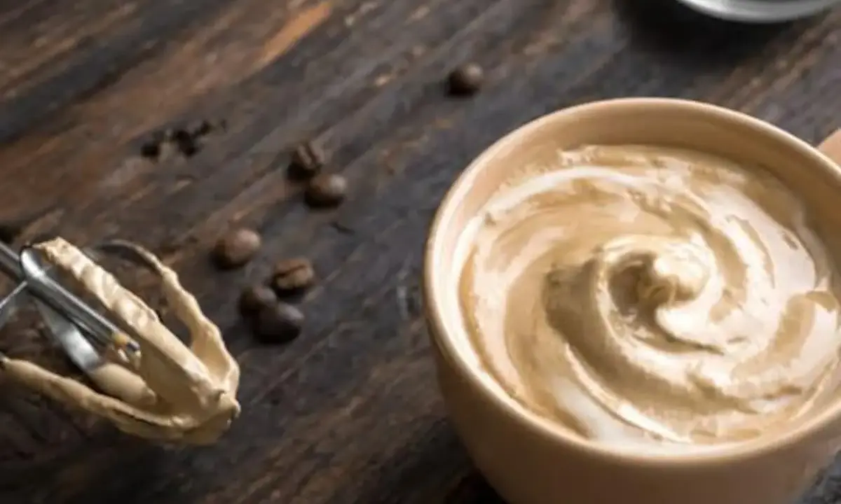 Cremige Crema al Caffè in einer Tasse, daneben ein Handmixer mit Teigresten und Kaffeebohnen auf Holz.