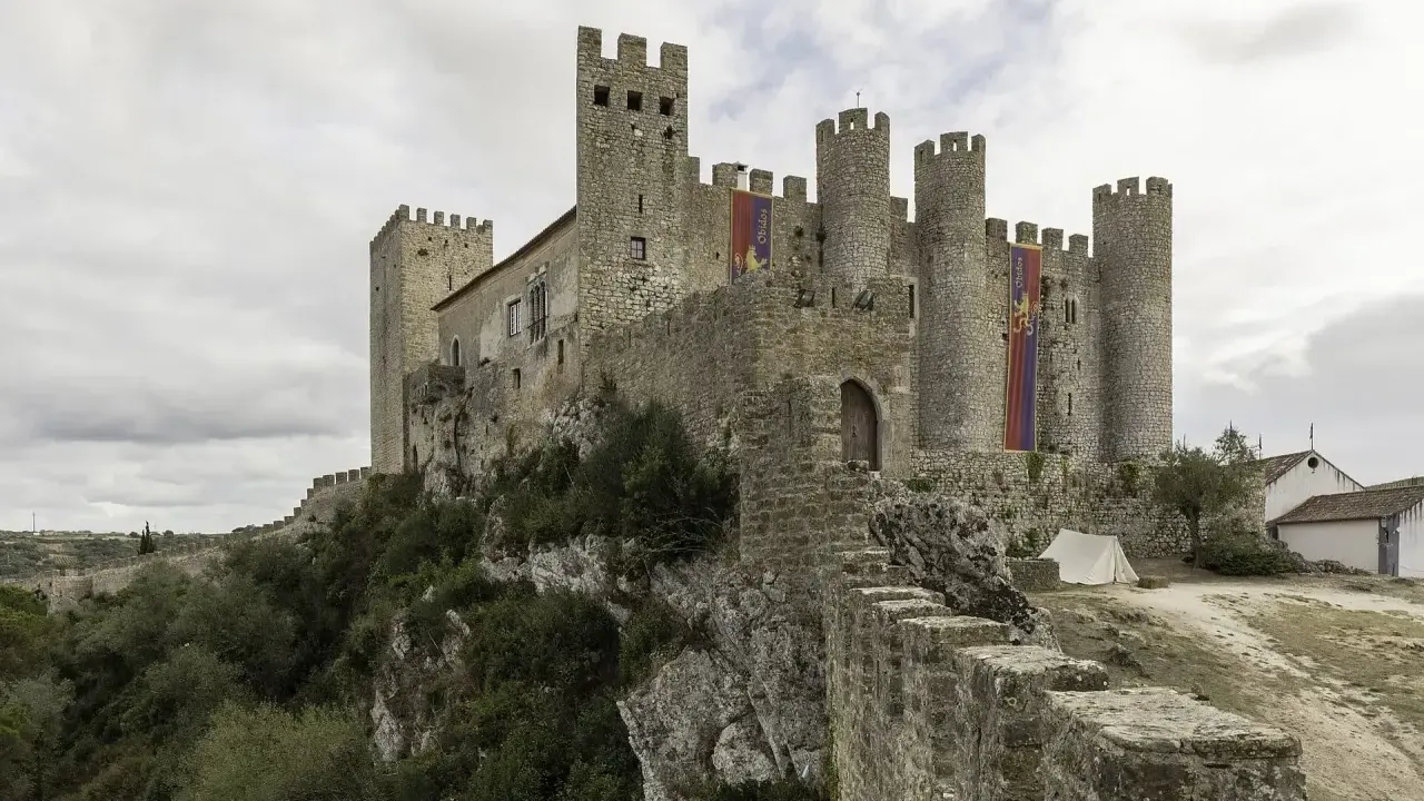 Die Obidos Burg thront majestätisch auf einem Felsen. Fahnen mit dem Namen "Obidos" wehen im Wind.
