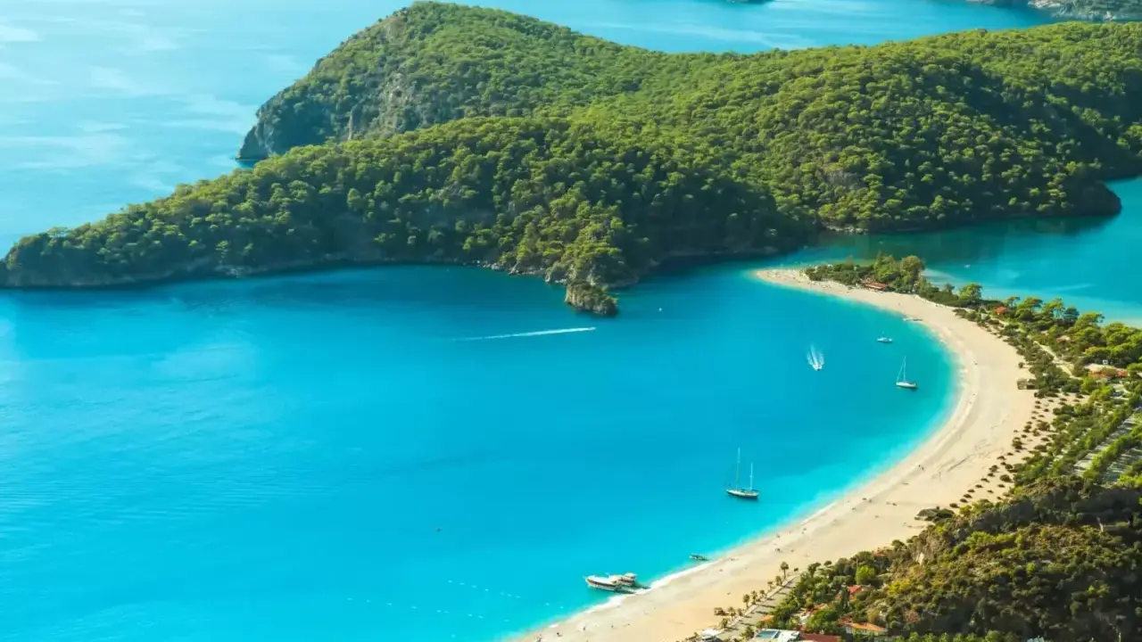 Idealne miejsce, gdzie jechać w niedzielę: turkusowa zatoka, piaszczysta plaża, zielone wzgórza i żaglówki.