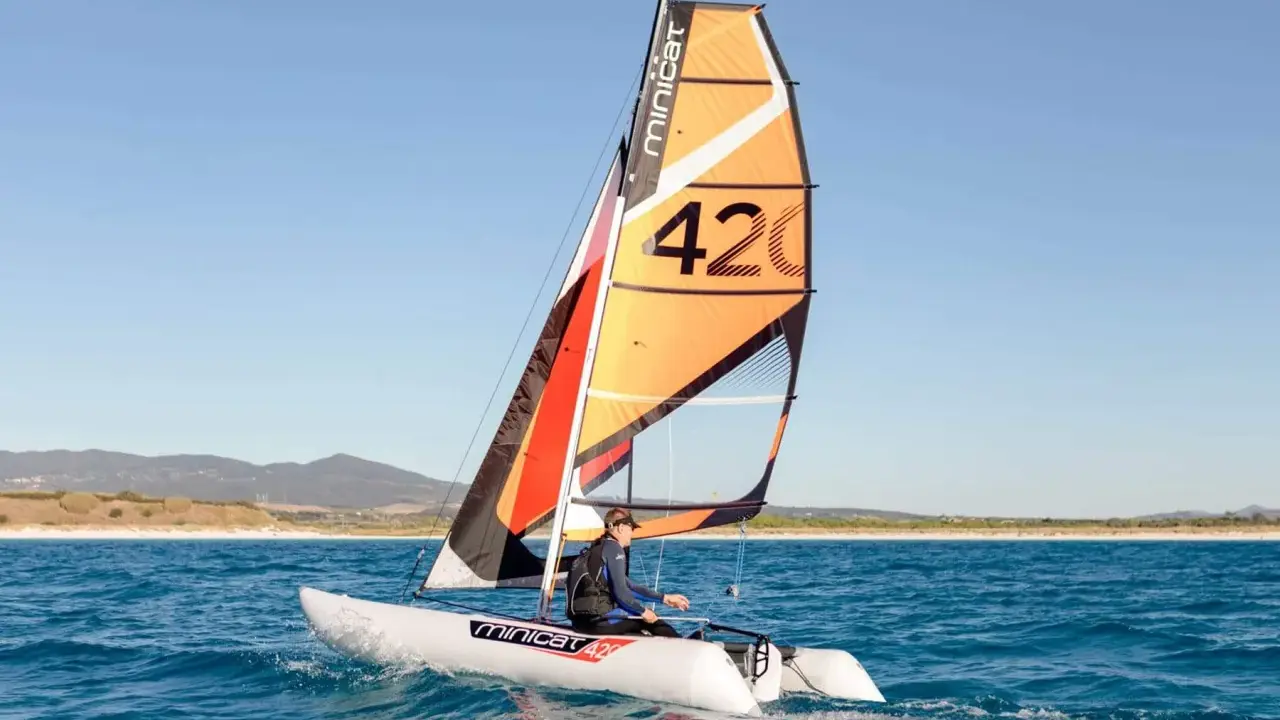 Un catamaran berny cat navigue sur une mer bleue, avec une voile orange et noire portant le numéro 42.