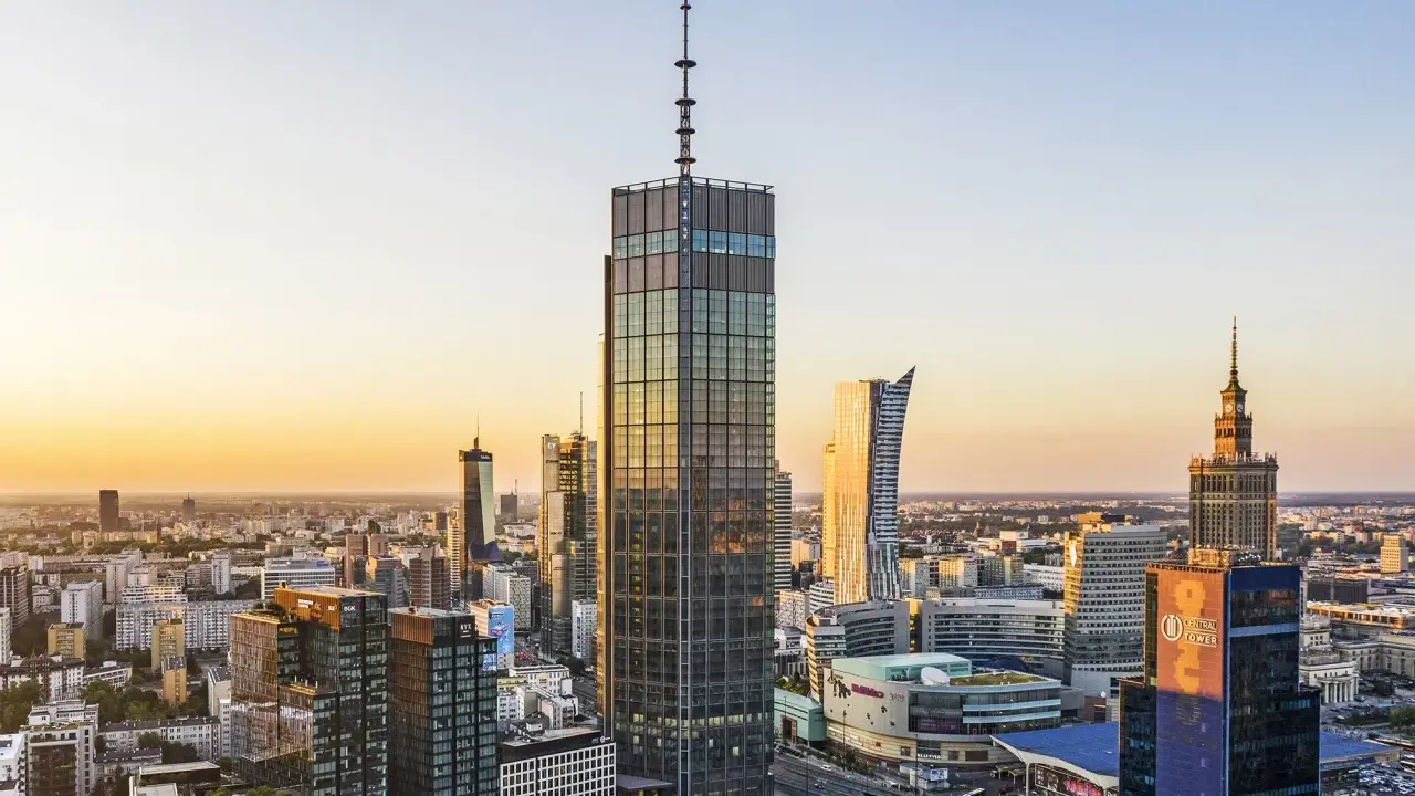 Warszawski krajobraz zdominowany przez wieżowce, w tym najwyższy hotel w Warszawie, lśni w złotym świetle zachodzącego słońca.