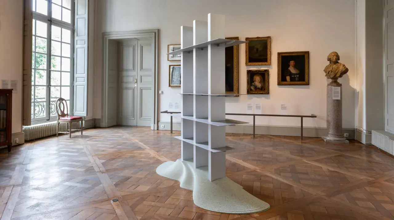 En modern skulptur, som en hyllning till Gustav Winsth, står i ett rum med gamla målningar och en byst.