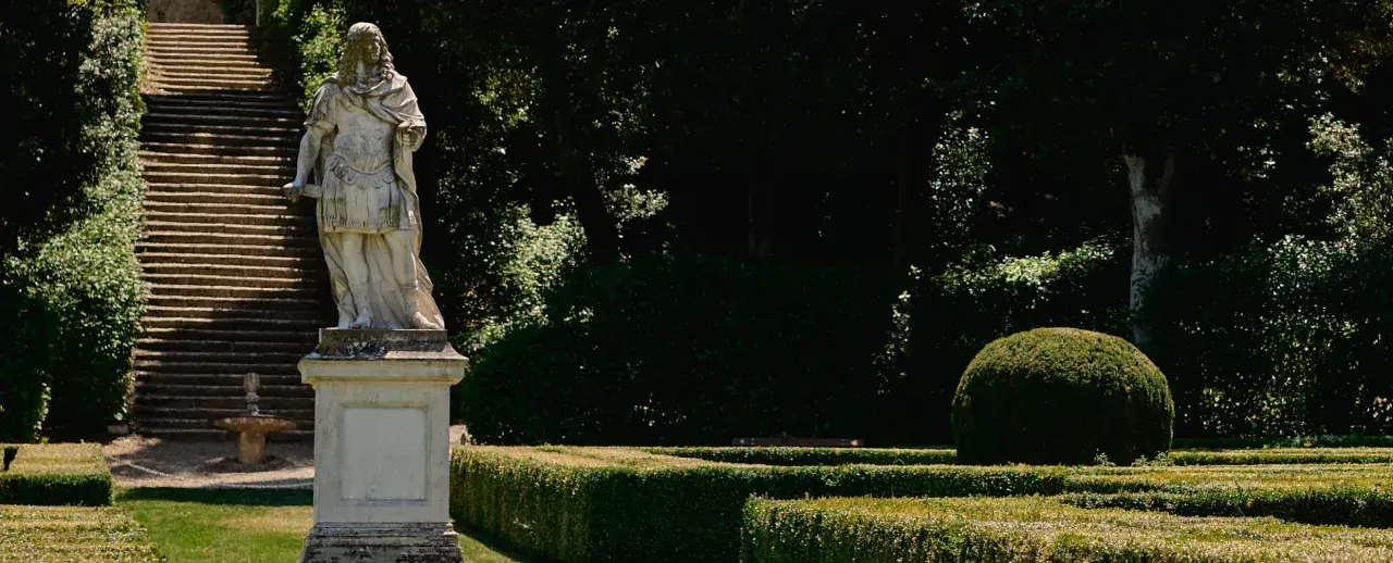 Statua romana domina la scalinata nei **Horti Leonini**. Giardini curati e alberi ombrosi creano un'atmosfera regale.