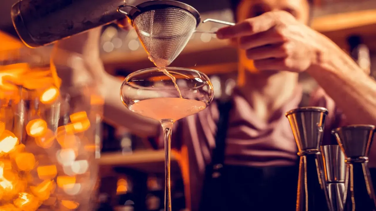 Un barman verse un cocktail d'un shaker dans un verre. C'est ainsi qu'un shaker sert à mélanger et refroidir les boissons.
