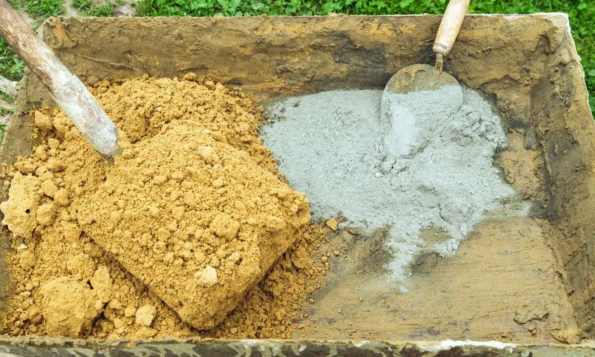 Brouette contenant du sable et du ciment, prêts pour le dosage béton. Une pelle est dans le sable, une truelle dans le ciment.