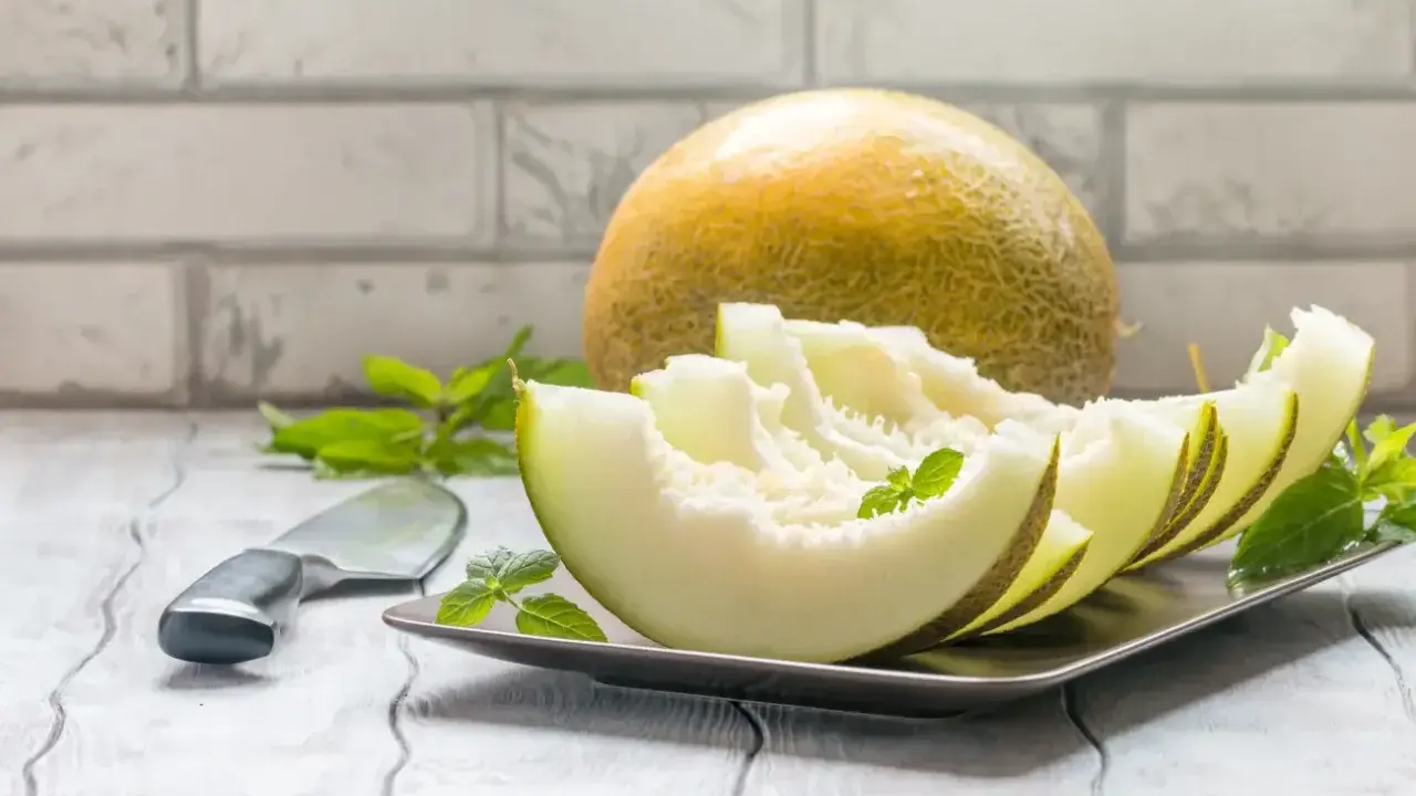 Kawałki melona na talerzu, obok cały owoc i nóż. Niska wartość melon indeks glikemiczny.