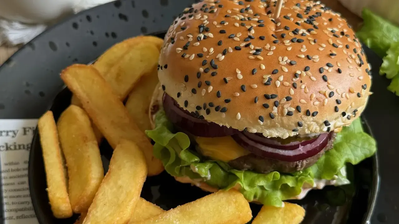 Soczysty burger wołowy z frytkami na czarnym talerzu.