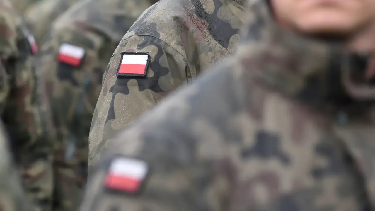 Żołnierze w mundurach moro, z polskimi flagami na ramionach, czekają na swoją emeryturę wojskową.