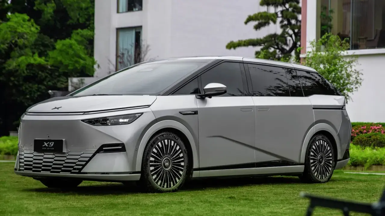 Le Xpeng X9, un monospace argenté futuriste, est garé sur une pelouse verte devant un bâtiment moderne.